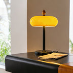 The lamp from Clérachic lit up, with the whole glass dome a bright honey yellow, on a black table next to a newspaper.
