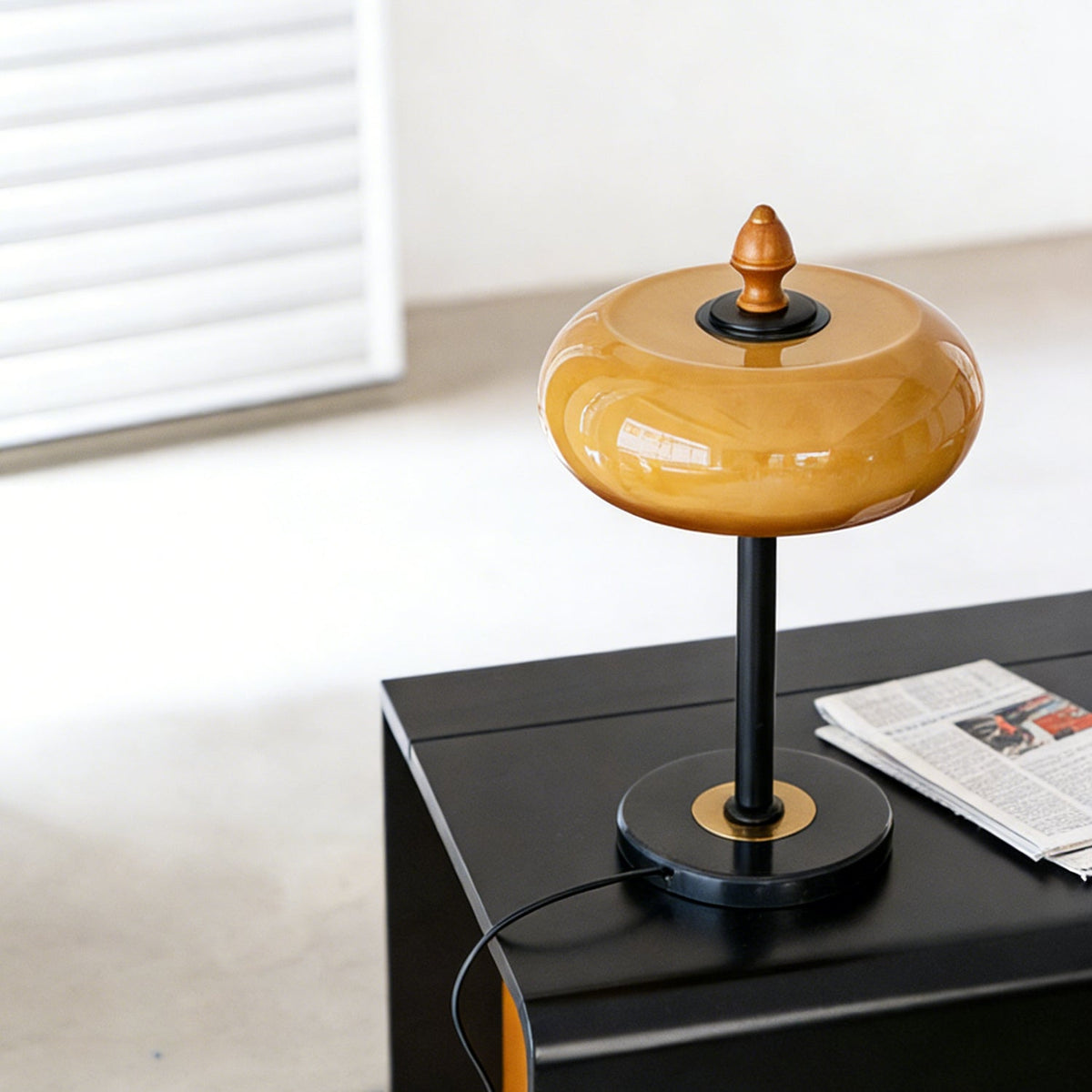 High angle on the Clérachic lamp's glass dome and wooden finial, with its cord running off the black table edge.