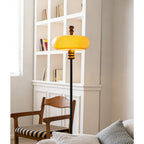 The caramel glass shade glows bright yellow-orange beside white shelving and a wooden chair with a striped seat, from Clérachic.