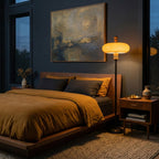 This Clérachic floor lamp stands by a low wooden bed with mustard linen in a dark blue bedroom, its shade lit warm.