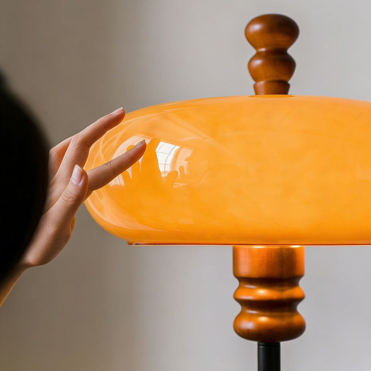 Close view of a hand touching the smooth caramel glass shade and turned wooden finial of this Clérachic floor lamp.