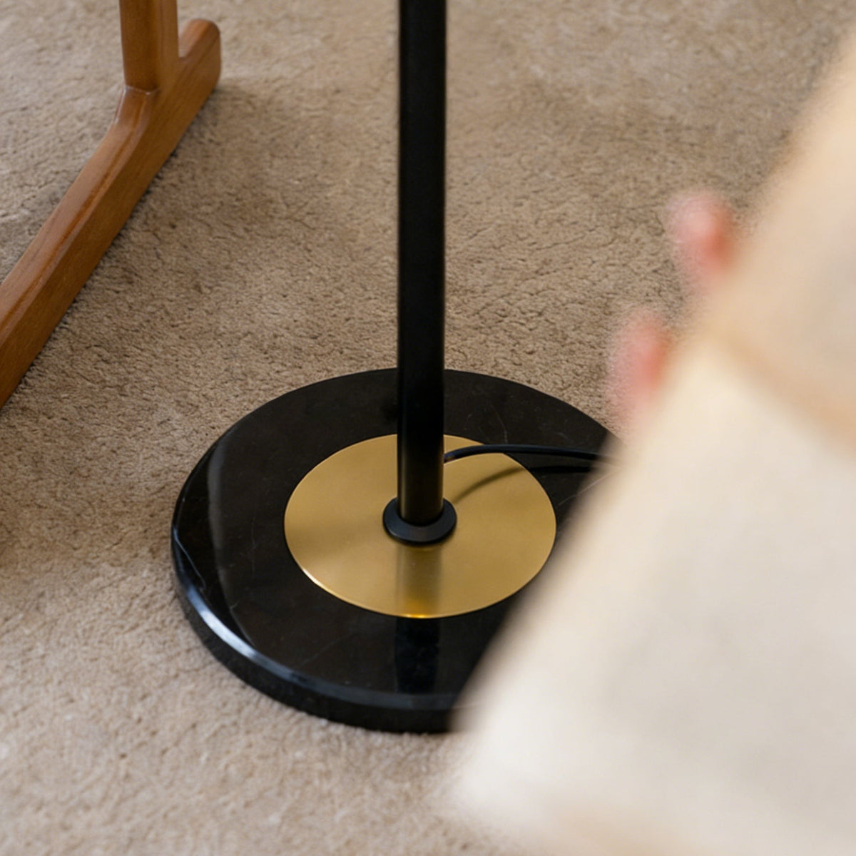Close view of the round black marble base, brass disc and black stem of this Clérachic floor lamp, standing on a carpet.
