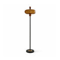 Clérachic floor lamp with a caramel glass shade on a slim black stem and a round black base with a brass centre, on white.