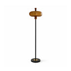 Clérachic floor lamp with a caramel glass shade on a slim black stem and a round black base with a brass centre, on white.