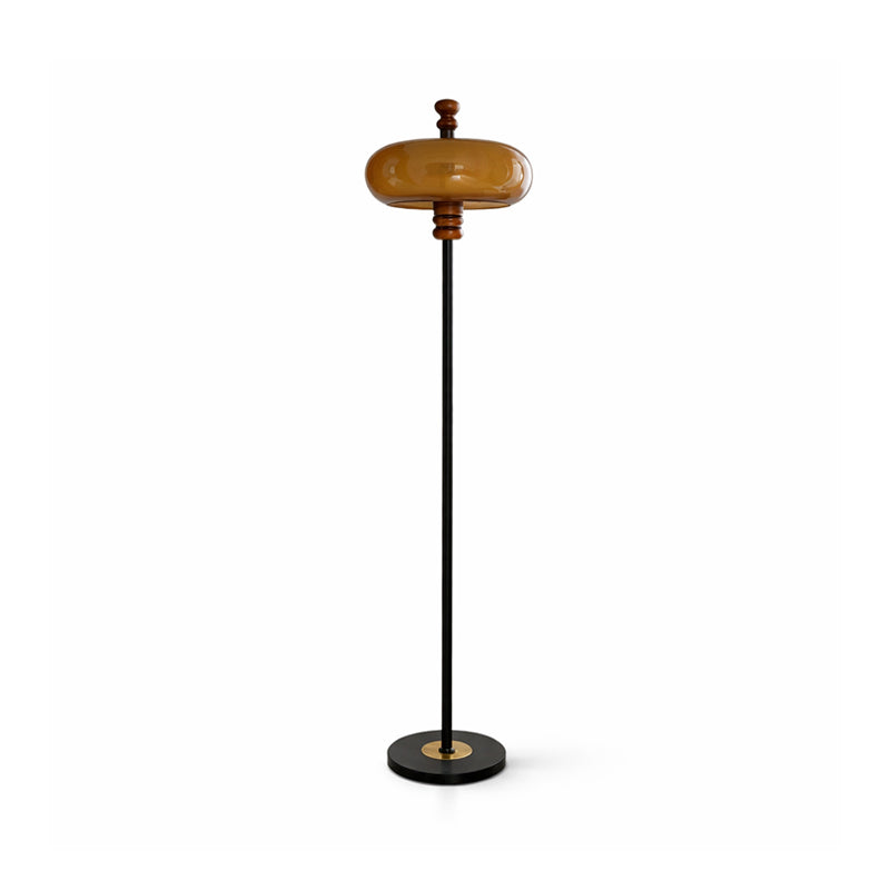 Clérachic floor lamp with a caramel glass shade on a slim black stem and a round black base with a brass centre, on white.