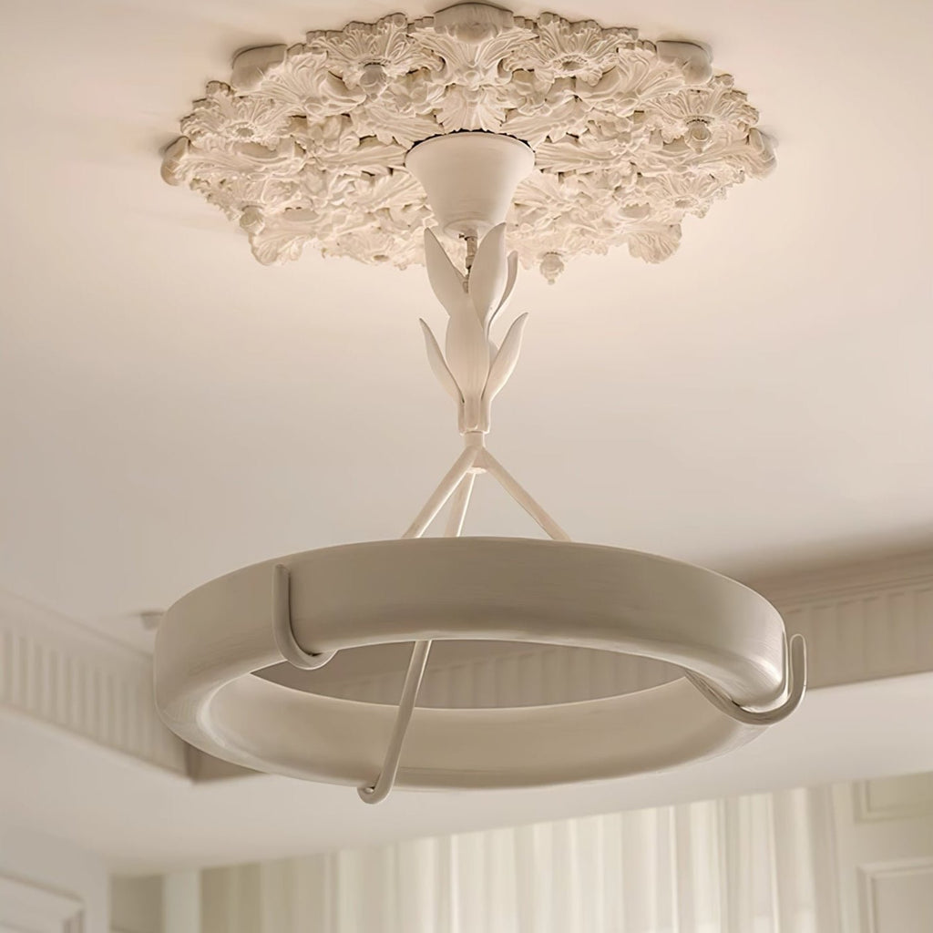 Close upward view of the white plaster ring and its curved hooks beneath an ornate ceiling medallion, on a Clérachic chandelier.