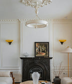 This Clérachic chandelier hangs from a plaster ceiling rose in a white panelled room with a black cast-iron fireplace and a pair of amber wall lights.