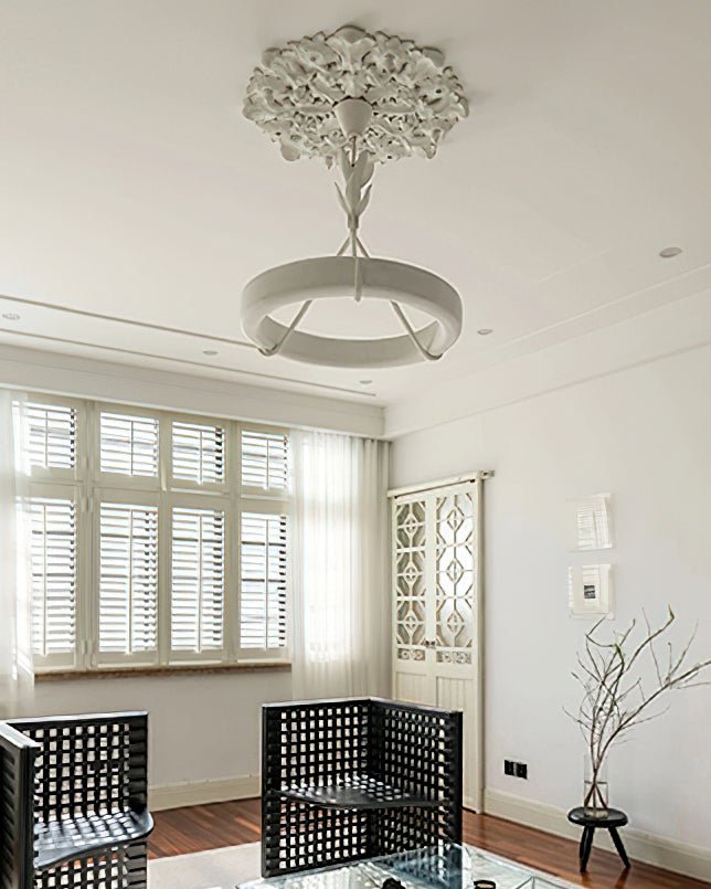 From a distance, a Clérachic chandelier hangs under a carved plaster rose in a bright room with louvred shutters and black lattice armchairs.
