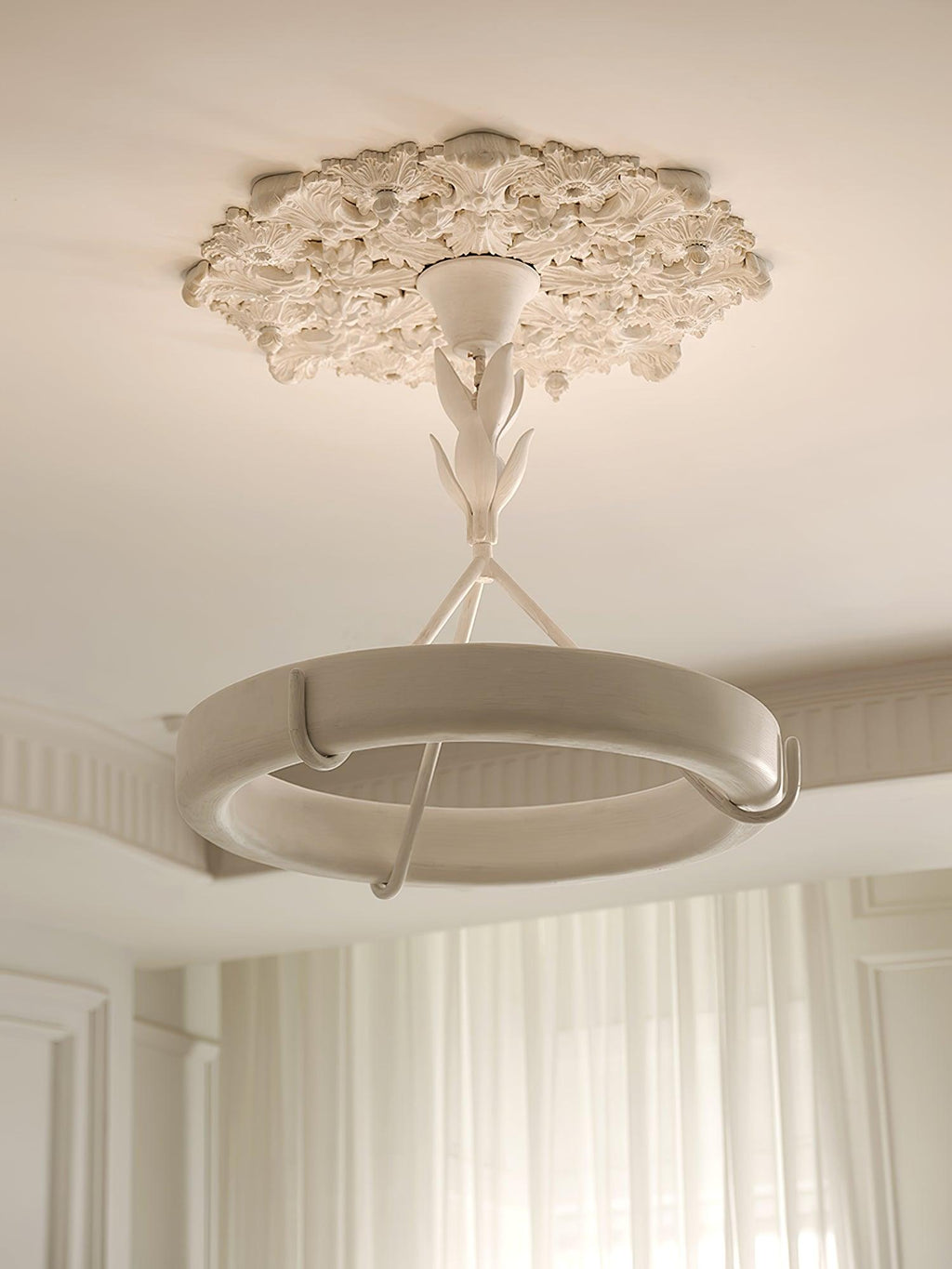 Looking up at this Clérachic chandelier from beneath a plaster ceiling rose, with the white ring and its hooks in front of cream curtains.