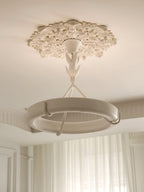 Looking up at this Clérachic chandelier from beneath a plaster ceiling rose, with the white ring and its hooks in front of cream curtains.