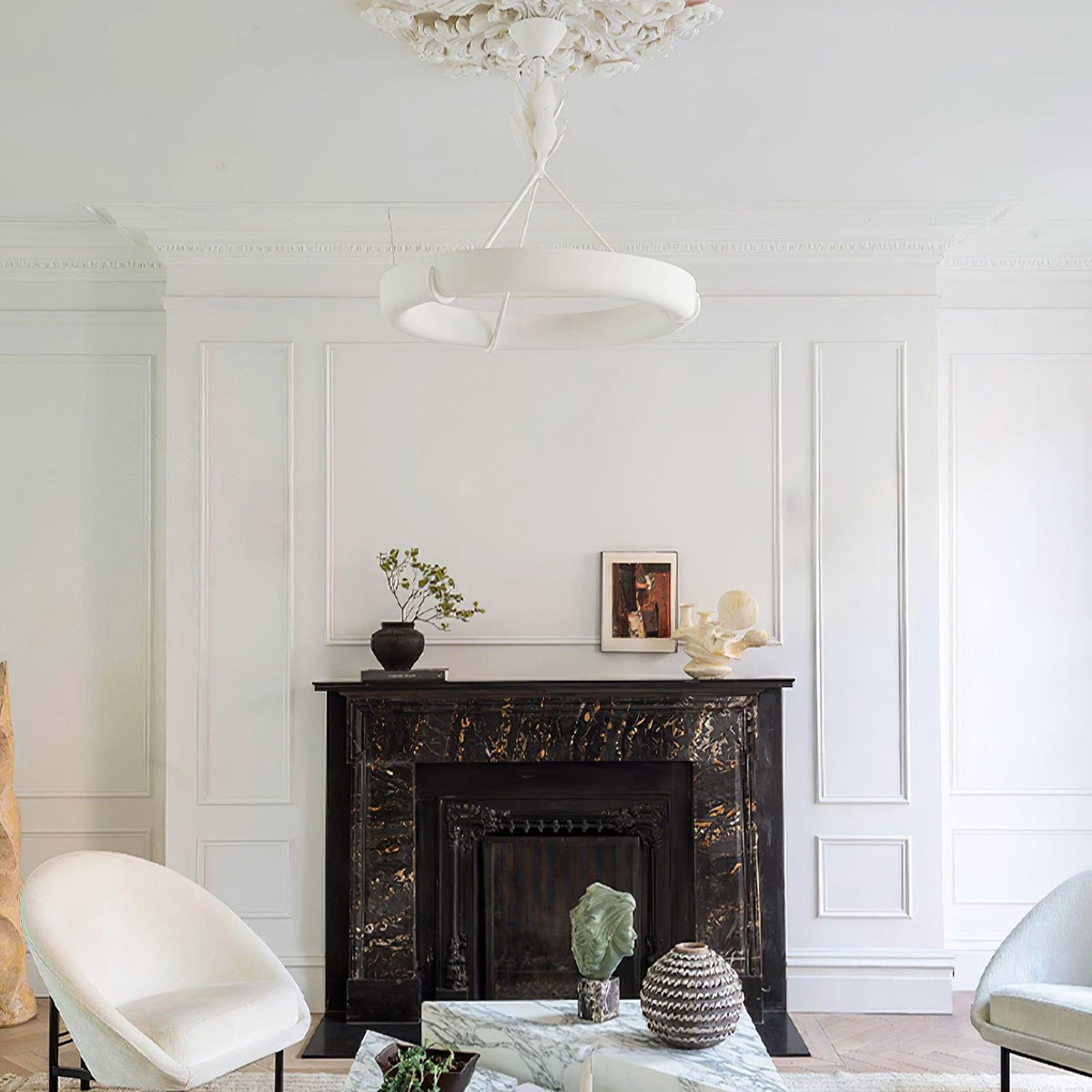 A Clérachic chandelier hangs in a white panelled room above a black marble fireplace, with a pair of white chairs below.
