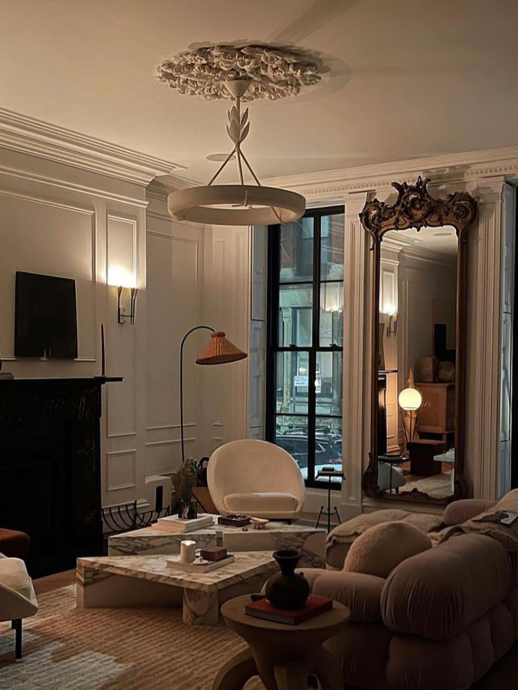 A warm, dim living room with a deep brown sofa and a gilded mirror, where this Clérachic chandelier hangs below a plaster rose.