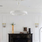 Close upward view of the white ring above a black marble fireplace with two brass wall lights; a Clérachic chandelier.