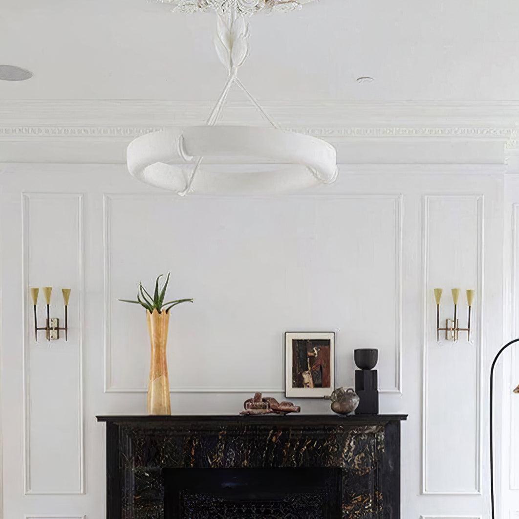 Close upward view of the white ring above a black marble fireplace with two brass wall lights; a Clérachic chandelier.