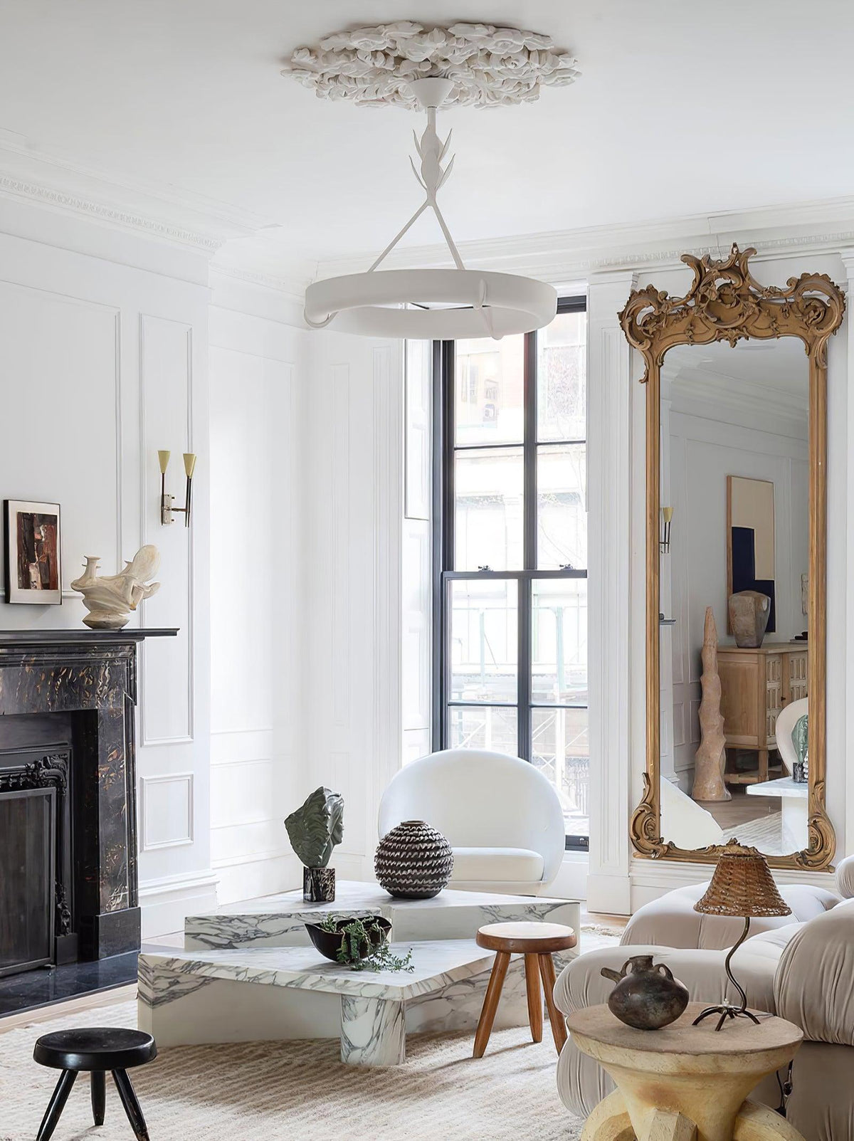 Tall view of a white living room with a window and gilded mirror, with this Clérachic chandelier hanging below a carved plaster rose.