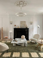 A green rug and a marble coffee table fill the floor below this Clérachic chandelier, which hangs centrally under a plaster rose.