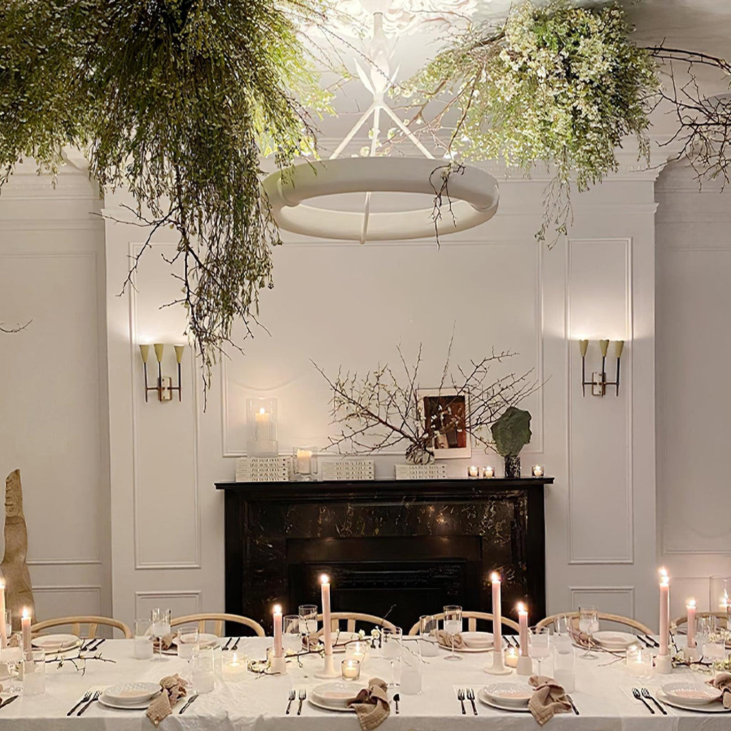 Close view of the white ring glowing under hanging greenery, above a candlelit table and a black fireplace; a Clérachic chandelier.