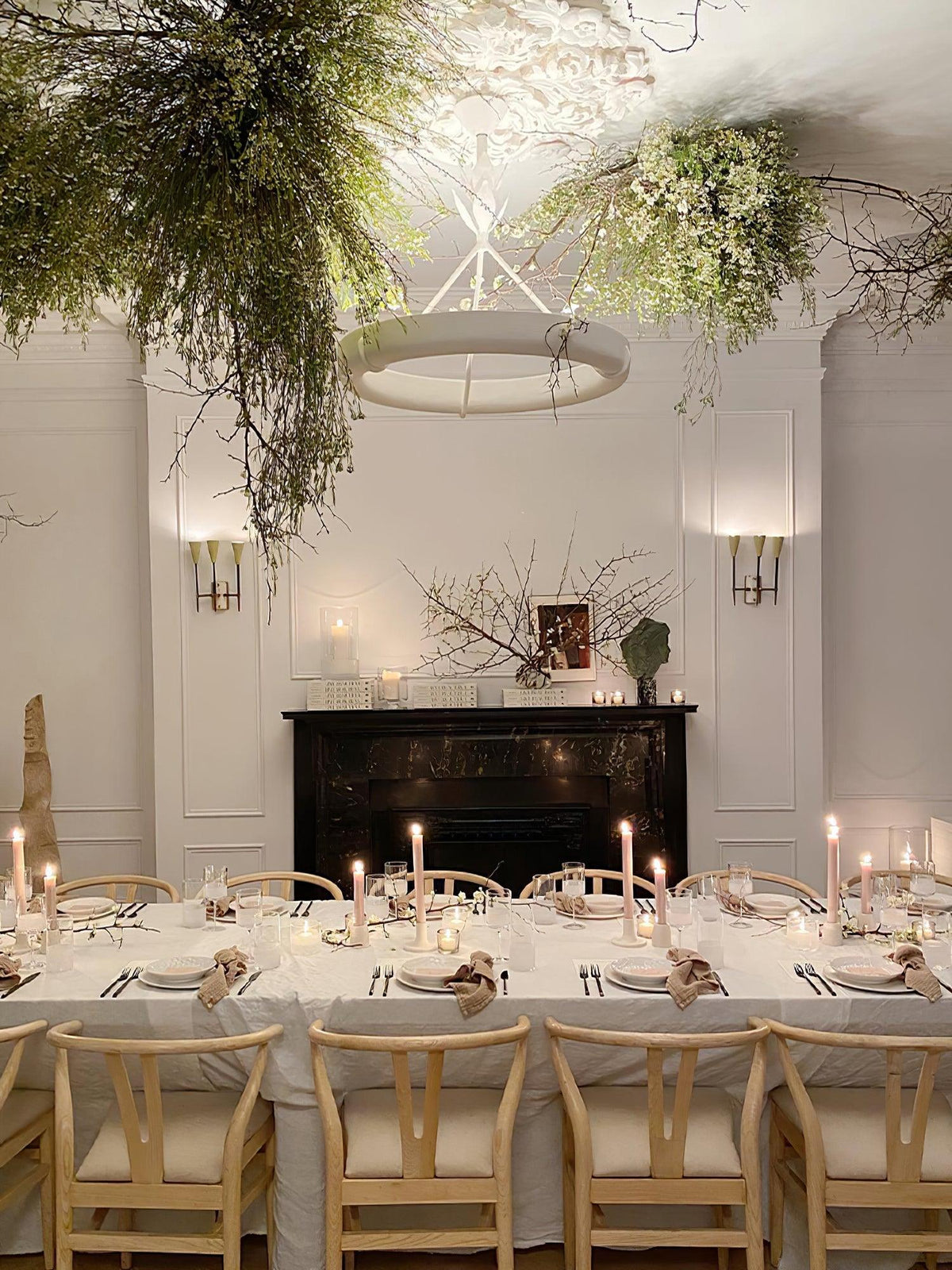 Dining room dressed with candles and light wood chairs, and this Clérachic chandelier hanging among branches overhead.