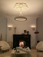By evening light, the plaster rose and white ring glow warmly above a fireplace with a lit fire; a Clérachic chandelier.