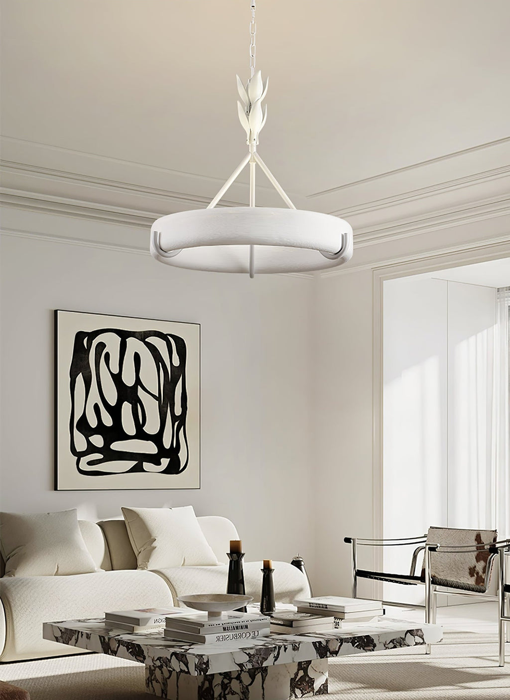 A white sofa, a marble coffee table and an abstract black-and-white print sit below this Clérachic chandelier in a bright, moulded room.