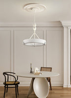 Dining corner with a round pale table and a cane-backed chair, with this Clérachic chandelier hanging from a ribbed rose above.