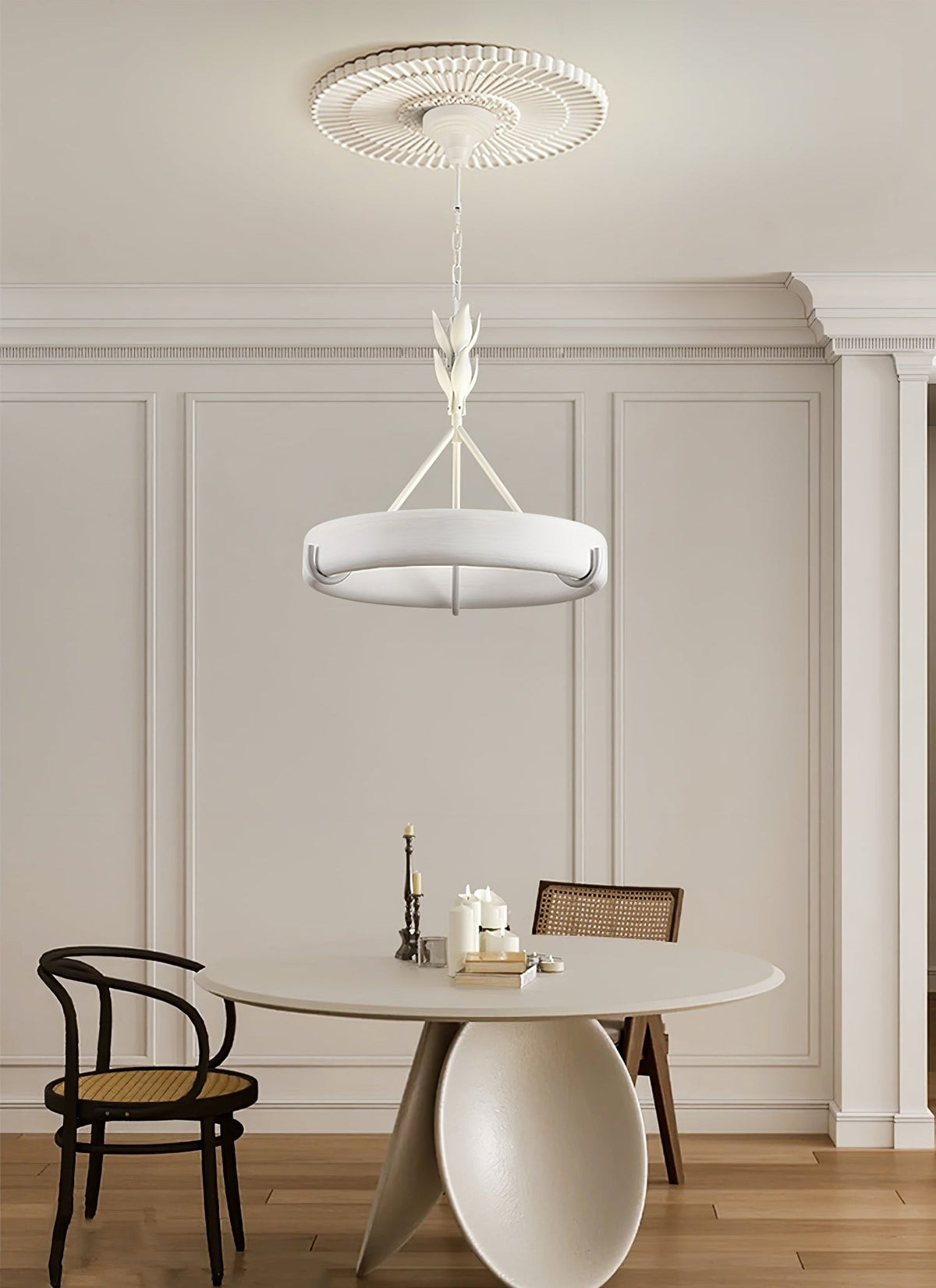 Dining corner with a round pale table and a cane-backed chair, with this Clérachic chandelier hanging from a ribbed rose above.