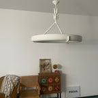 Same corner in warmer light, showing the matt white ring over a colourful tiled cabinet and a cane chair; a Clérachic chandelier.