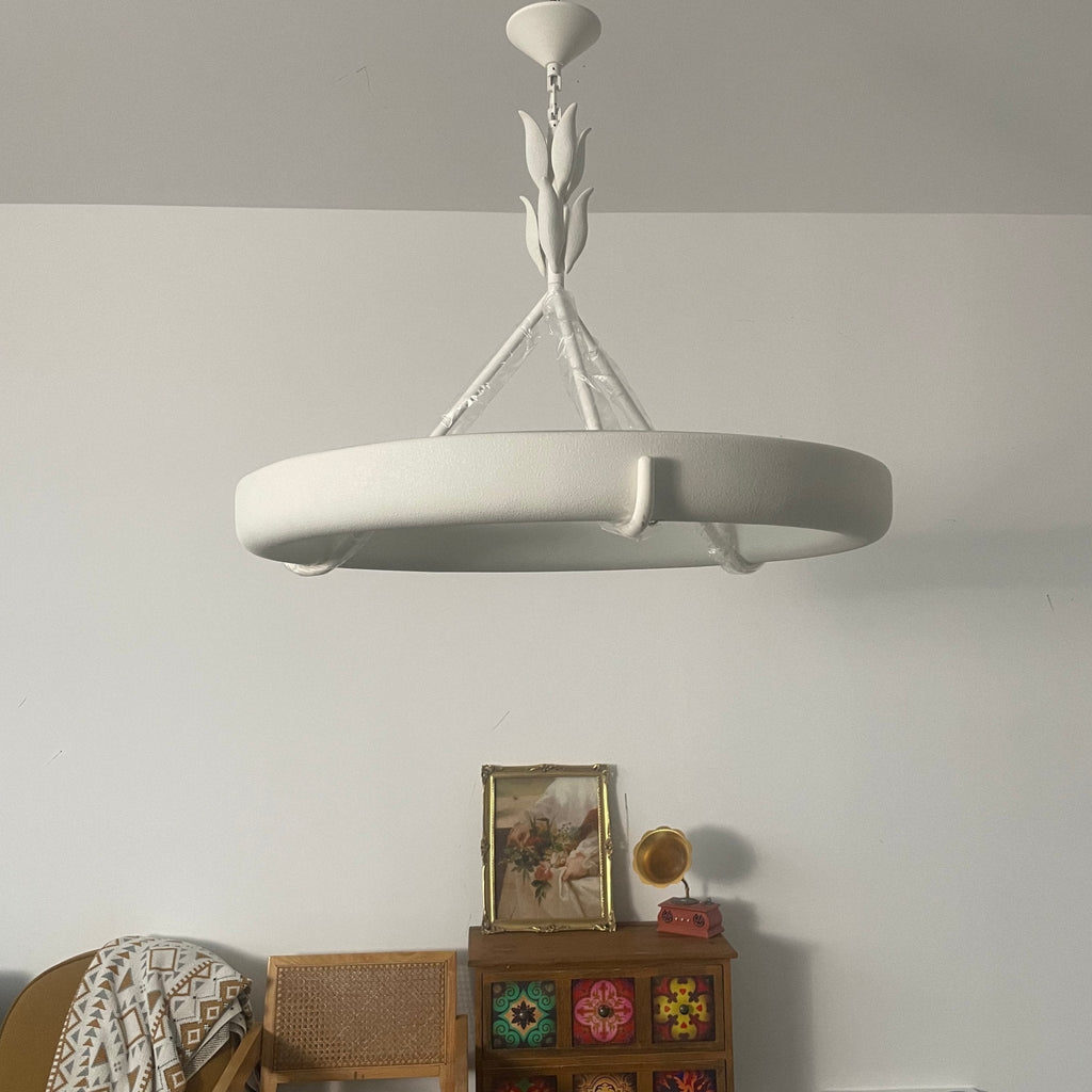Wide angle on the white ring and its curved hooks, hung low in front of a white wall; a Clérachic chandelier.