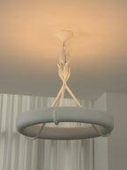 Amber ceiling light behind this Clérachic chandelier, showing the leaf-bud stem and ring against sheer curtains.