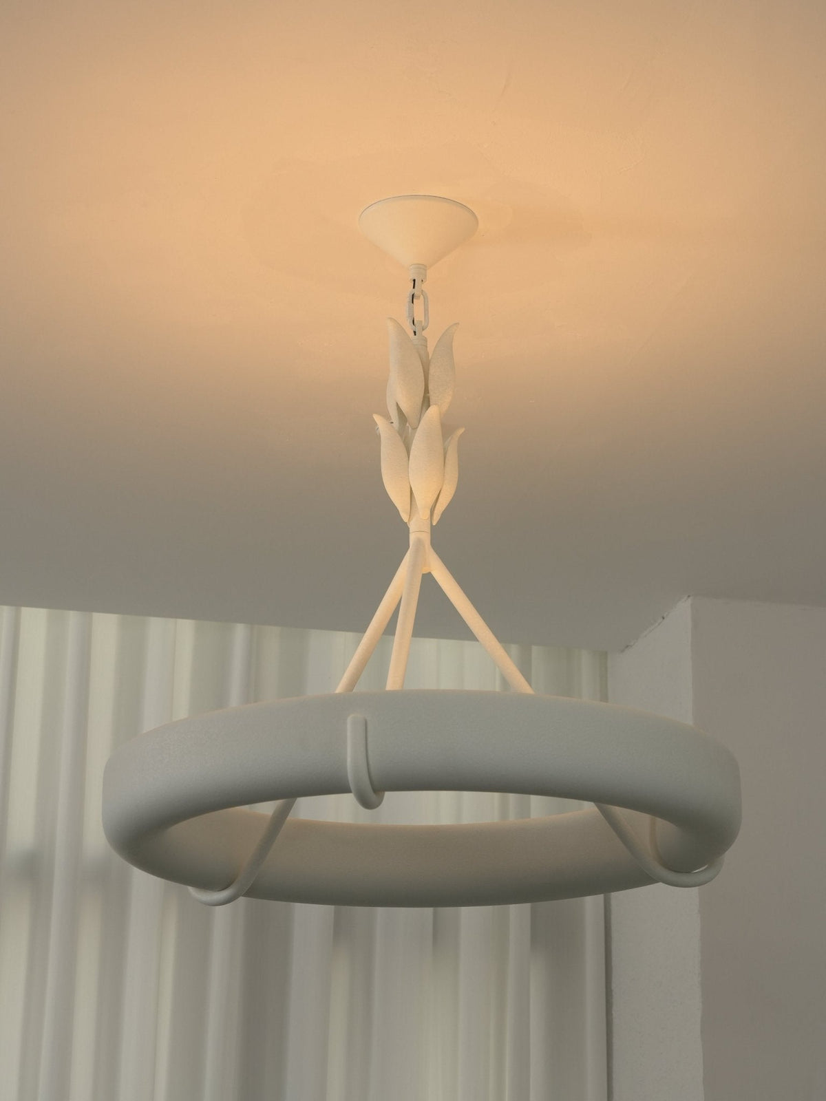 Amber ceiling light behind this Clérachic chandelier, showing the leaf-bud stem and ring against sheer curtains.