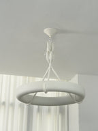 Cool daylight on the white ring, its leaf stem and ceiling cap, with curtains behind; a Clérachic chandelier.