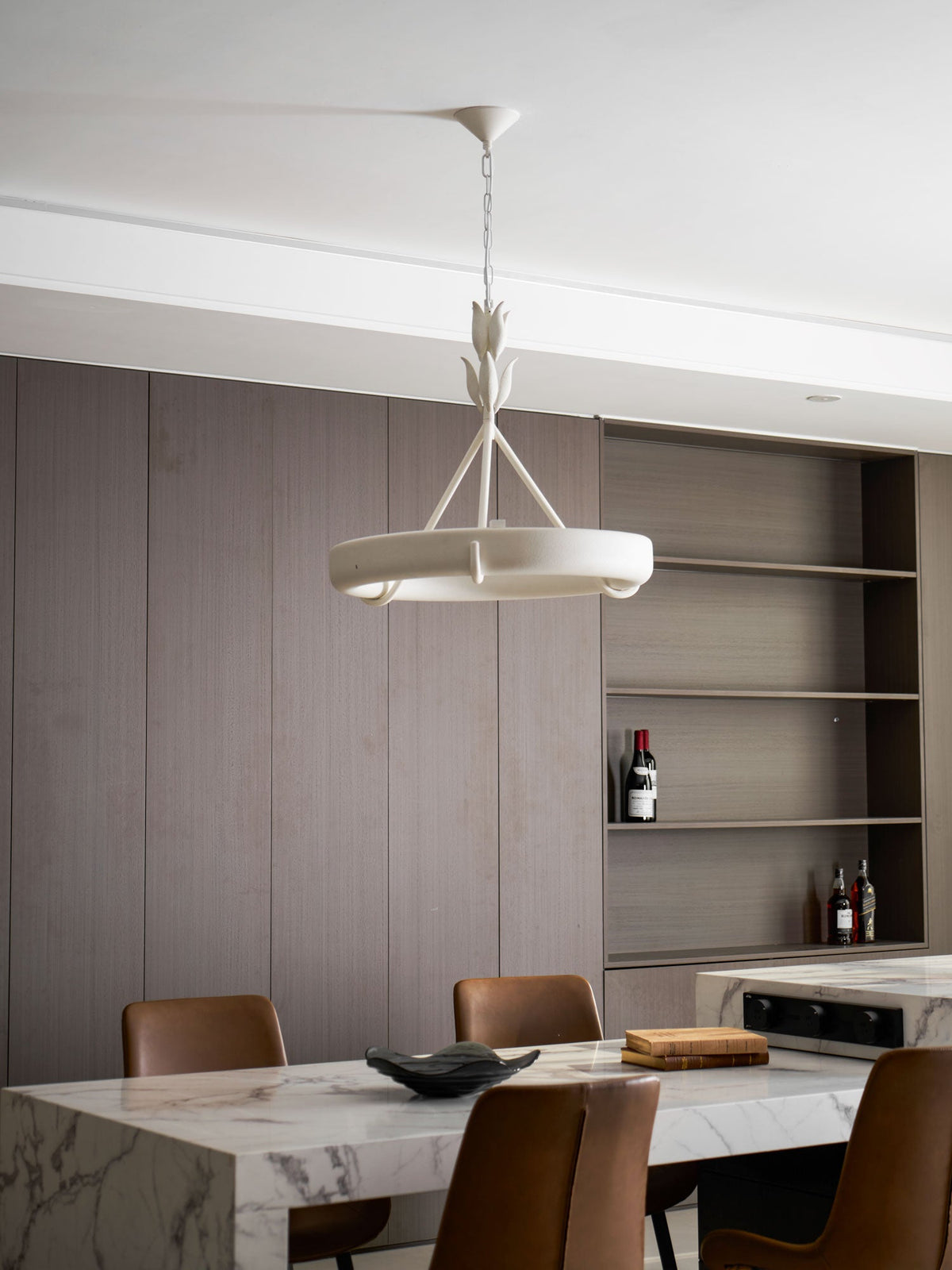 Side view of the white ring beside open shelving with a bottle of red wine, above a marble table; a Clérachic chandelier.