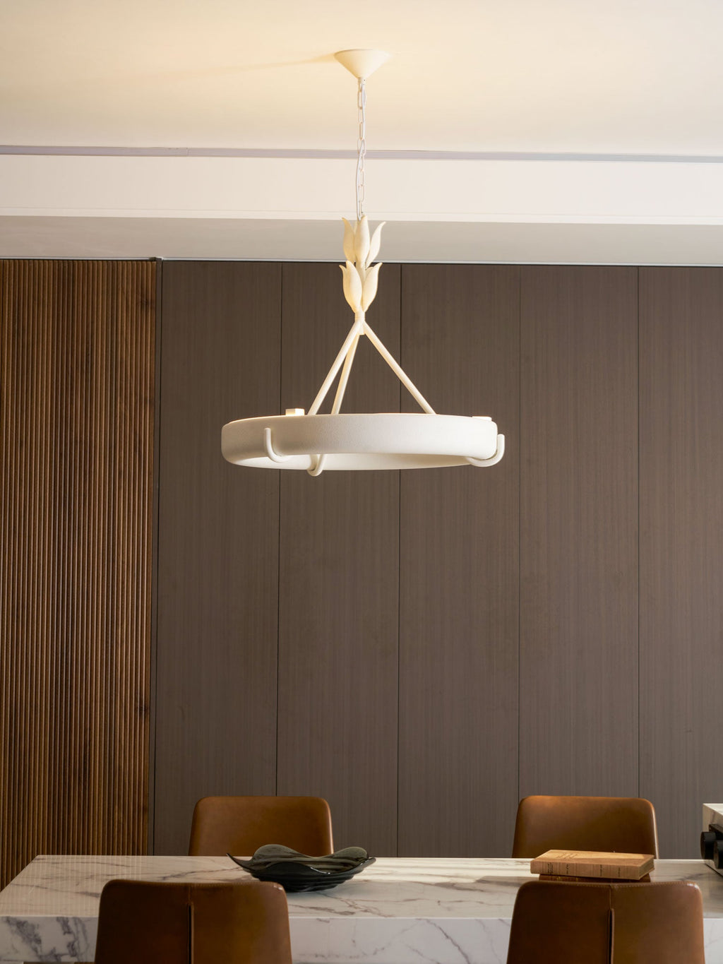 Pale ring and leaf stem against dark wood panelling, above leather chairs at a marble table; a Clérachic chandelier.