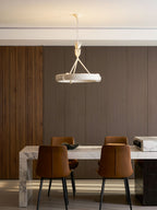 Pulled-back shot of the white ring above a marble dining table and two tan leather chairs with black legs; a Clérachic chandelier.