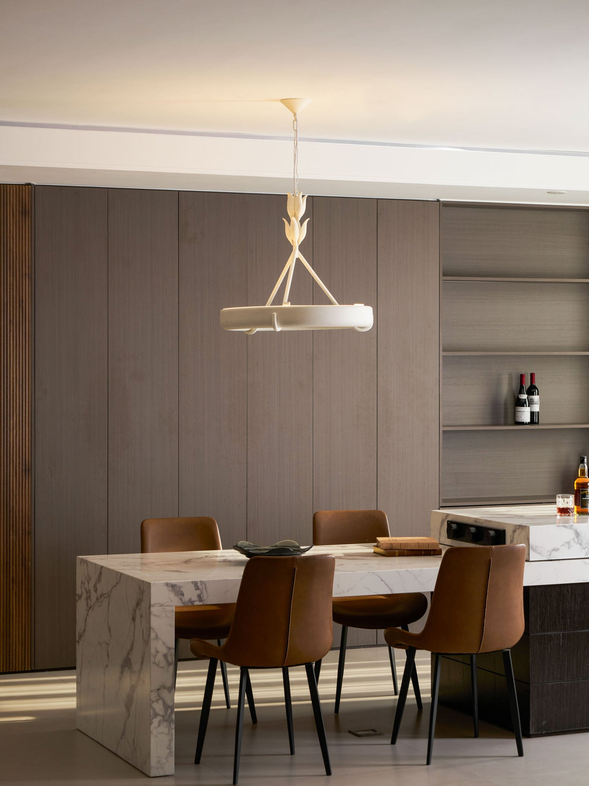 The white ring hangs before open shelves and a marble table with leather chairs, seen from further back; a Clérachic chandelier.