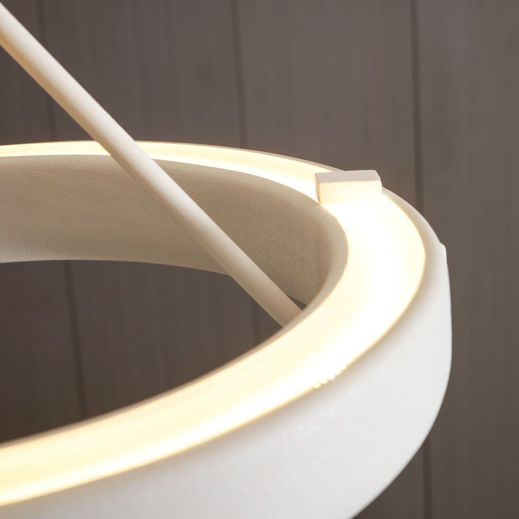 Close view of the glowing light strip inside the white ring, where a rod meets its edge on this Clérachic chandelier.