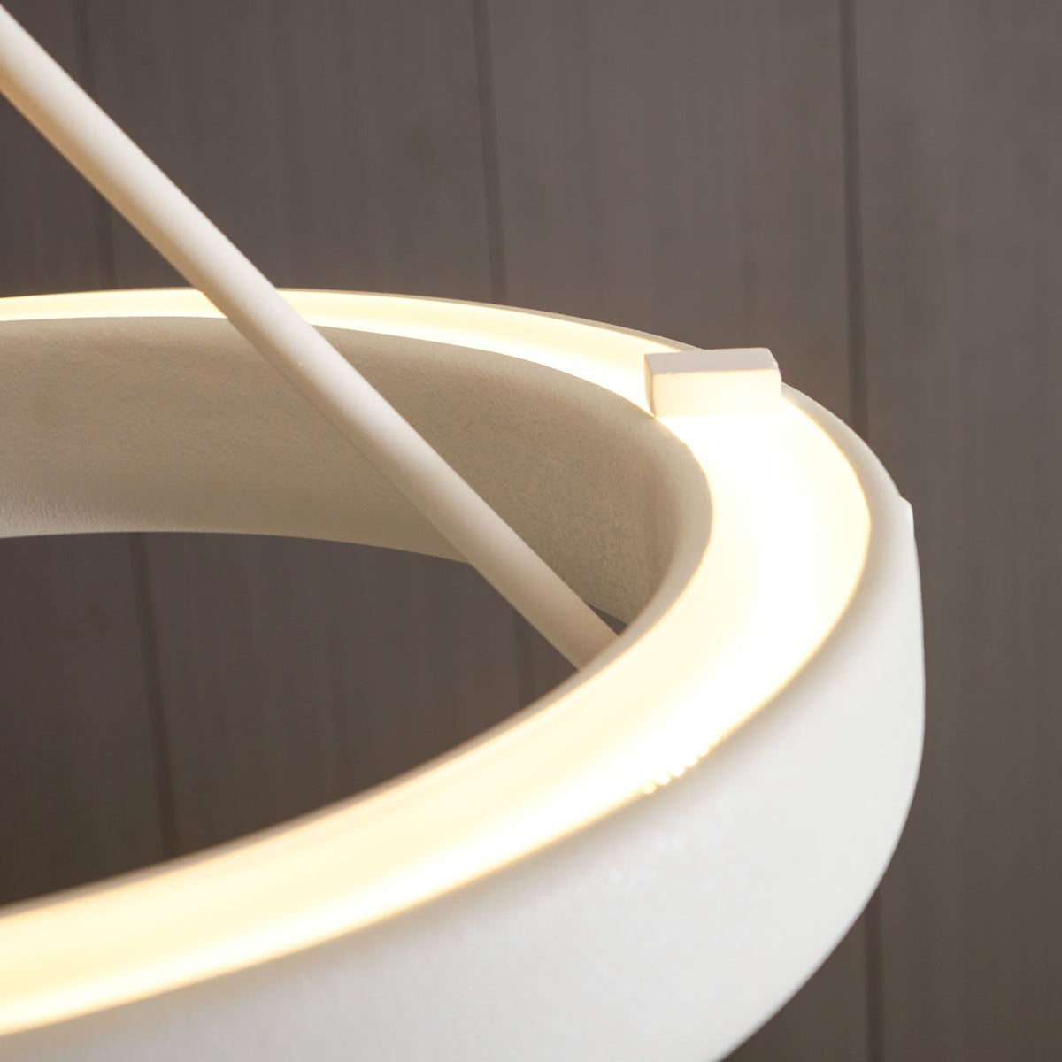 Close view of the glowing light strip inside the white ring, where a rod meets its edge on this Clérachic chandelier.