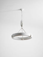Tilted studio view of the white ring showing its curved rim and one hook, against pale grey; a Clérachic chandelier.