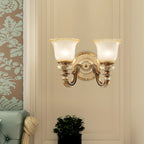 Double-head Clérachic wall light on a cream wall, with a damask-patterned wall at the left and a potted plant below.