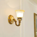 Lit single-head Clérachic wall light on a white wall, the amber-rimmed glass shade above a brighter gold backplate.