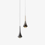 Two Clérachic pendants on thin cords, one in dark chrome with a flared body and one with a pale metal neck, on a plain backdrop.