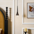 A single dark Clérachic pendant hangs by a bedside with a black carved bedpost, a framed poster and a candle holder.