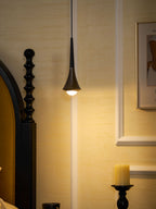 A black Clérachic pendant gives a warm light to a cream panelled wall, with a black bedpost and a candle below.