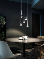 A small group of polished Clérachic drops hangs low above a round dark table set with a teapot and cups.