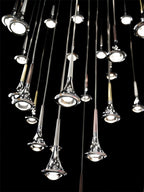 Close view of polished Clérachic drop pendants at varied heights, each with a round bulb in its flared base, on black.