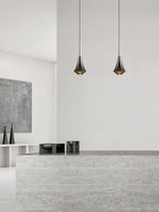 Two Clérachic pendants with tapered dark bodies hang side by side in front of a pale stone counter and white wall.
