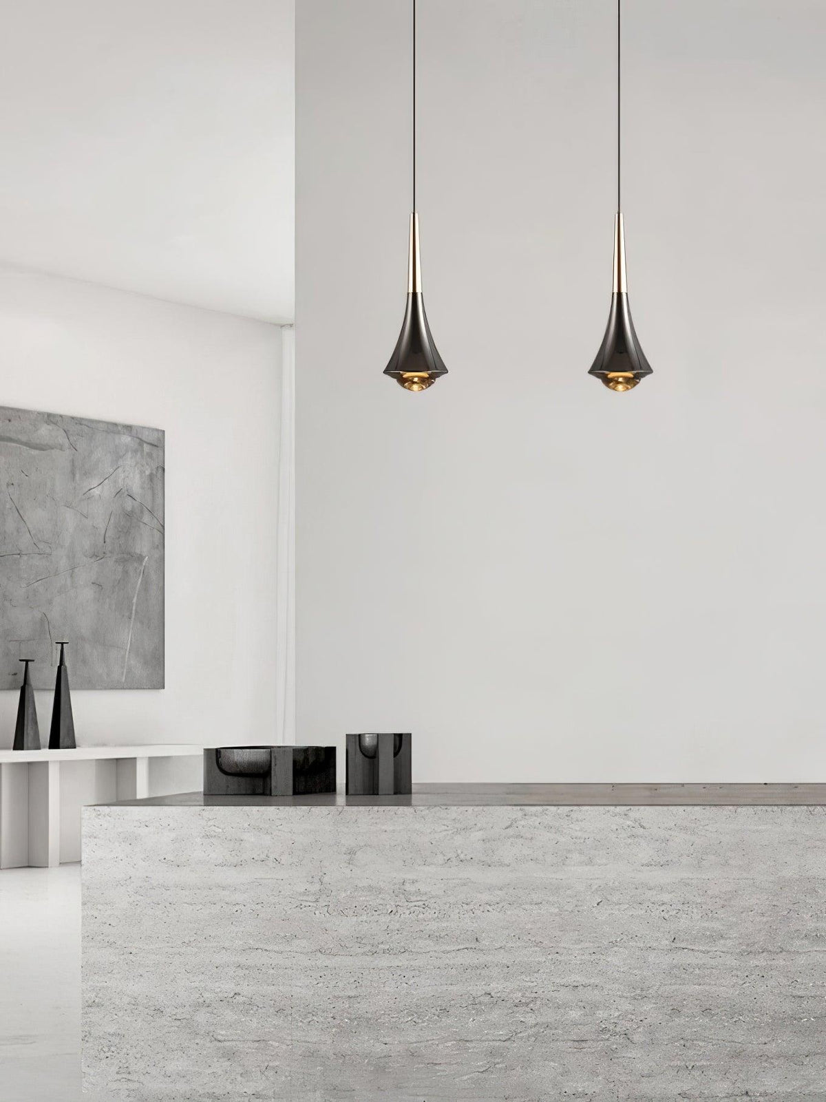 Two Clérachic pendants with tapered dark bodies hang side by side in front of a pale stone counter and white wall.