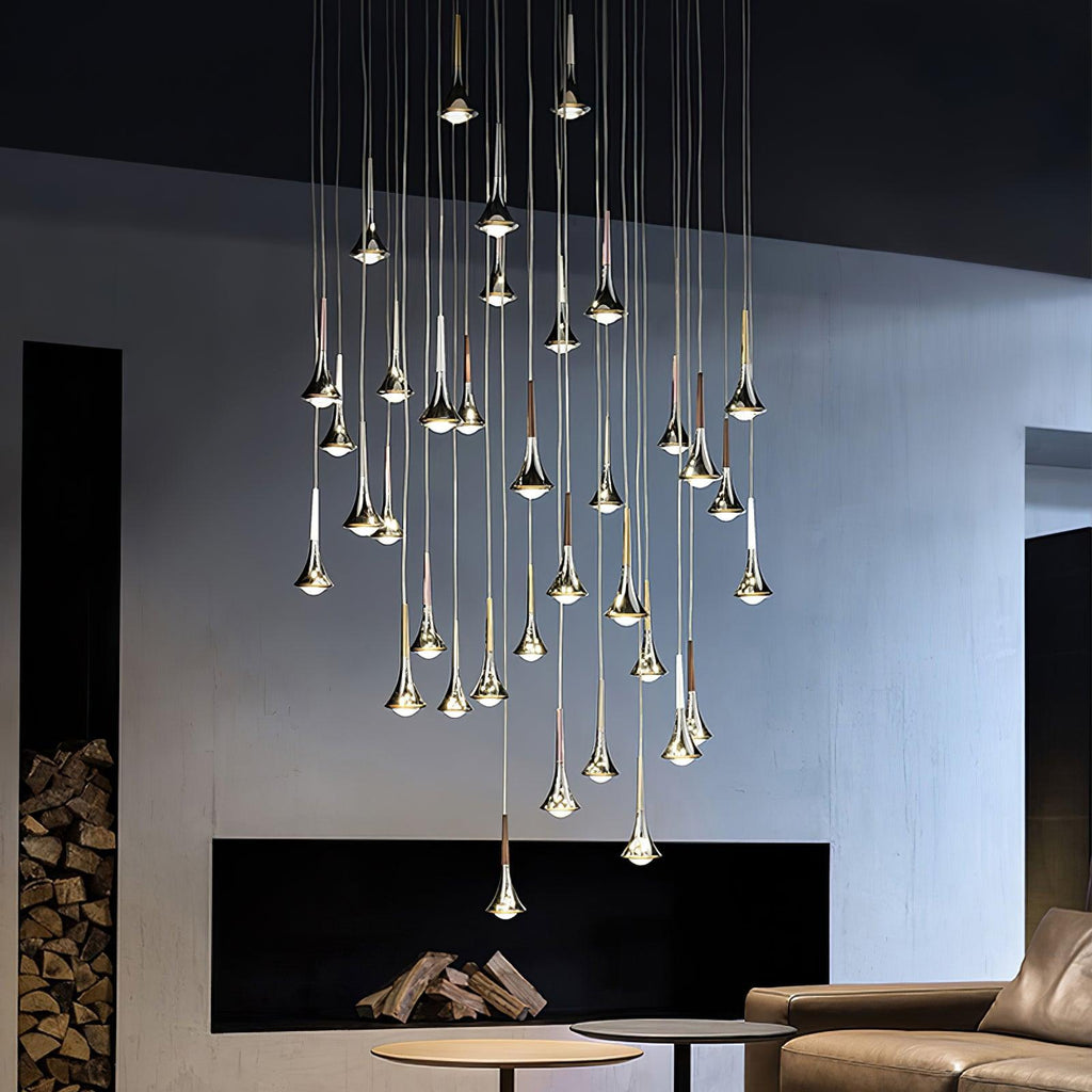 A cluster of Clérachic chrome drops at staggered heights, lit above a low table in a room with a black fireplace.