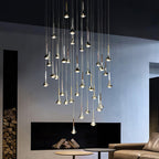 A cluster of Clérachic chrome drops at staggered heights, lit above a low table in a room with a black fireplace.