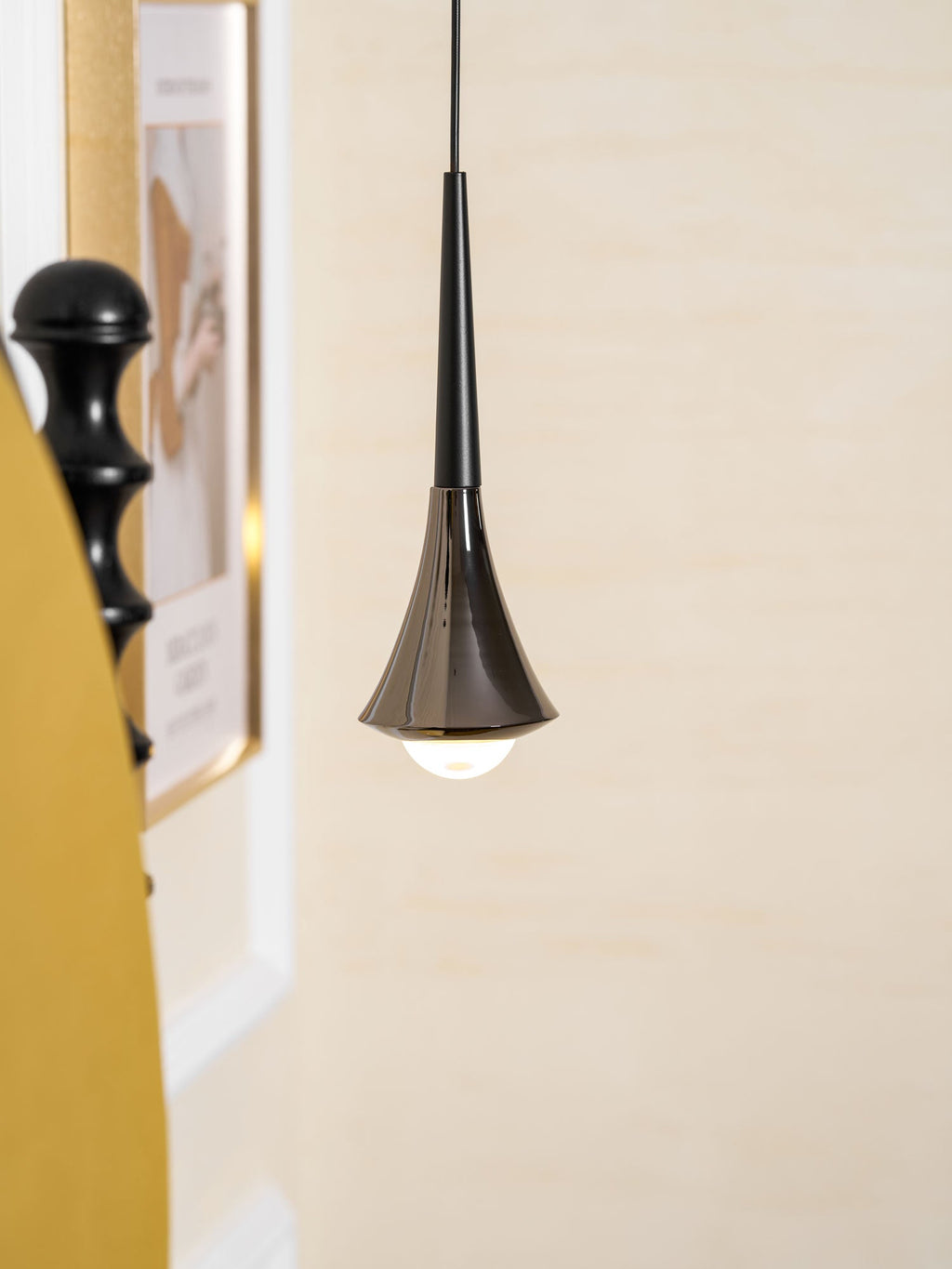 Close view of a flared black Clérachic pendant with an opal bulb below it, against a cream wall with a framed print.